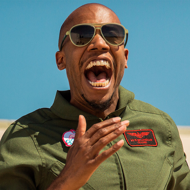 Un uomo con una tuta verde in stile militare e occhiali da sole aviatore verde cadetto con lenti verdi sfumate grida con gioia.