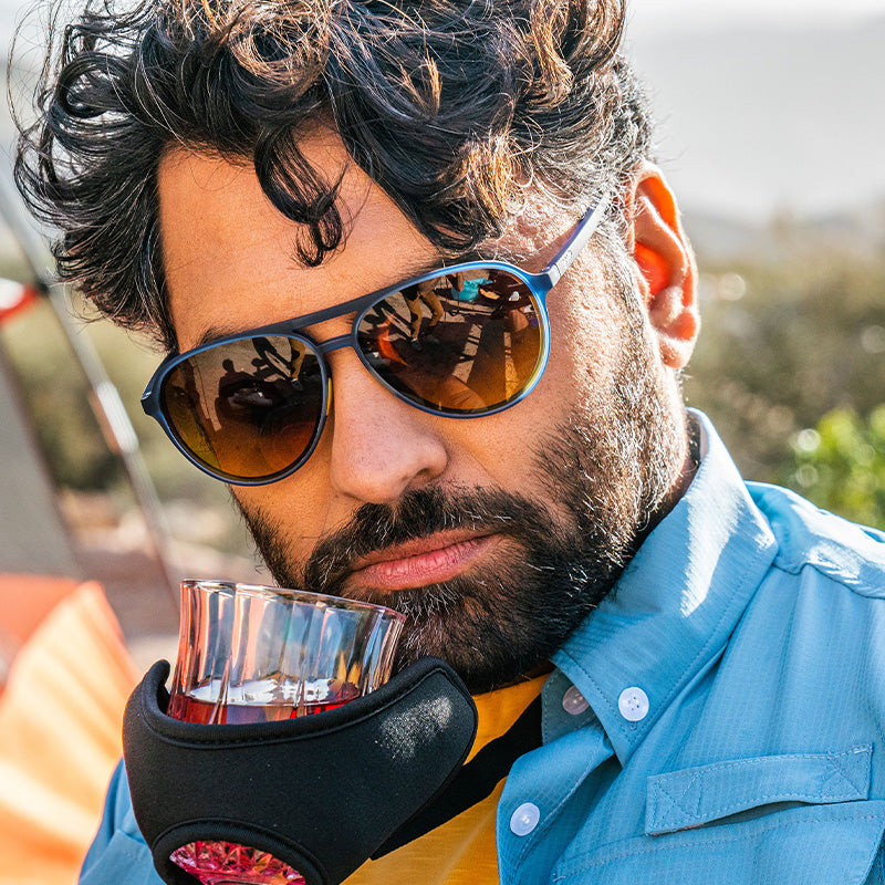 Un uomo barbuto con occhiali da sole blu da aviatore annusa il whisky da un aggeggio che regge un bicchiere che si potrebbe vedere in un catalogo Skymall.