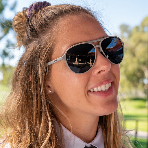Una donna sorridente in camicia a colletto in un club di golf indossa occhiali da sole grigi da aviatore con lenti non riflettenti.